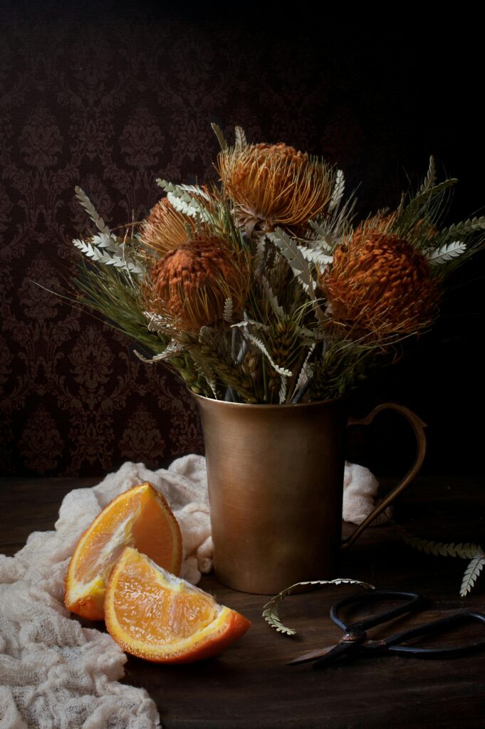 Artistic arrangement of dried flowers in a metallic vase with sliced oranges on a rustic table.